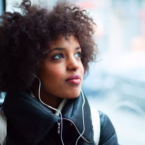 Foto: Ein junges Mädchen mit krausem Haar hört in einem öffentlichen Verkehrsmittel Musik.