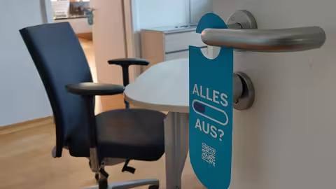 Der im folgenden Text beschriebene Türklinkenhänger hängt an einer Bürotür, die halb geöffnet ist.