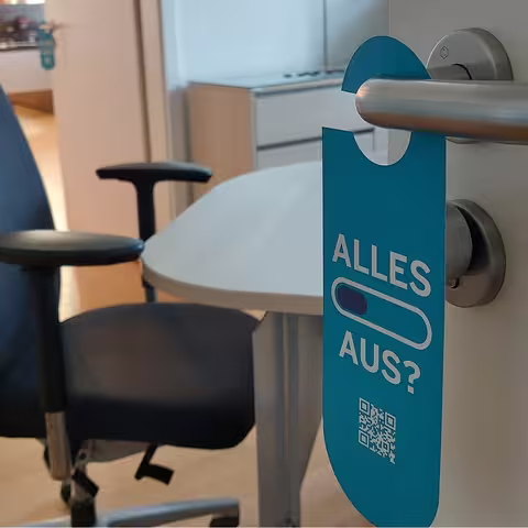 Der im folgenden Text beschriebene Türklinkenhänger hängt an einer Bürotür, die halb geöffnet ist.