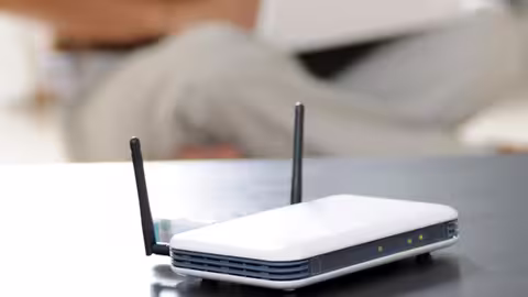 Foto: ein WLAN-Router auf einem Tisch, dahinter schemenhaft ein Internetnutzer