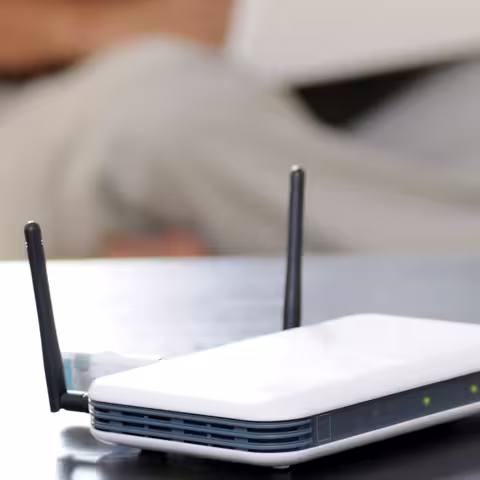 Foto: ein WLAN-Router auf einem Tisch, dahinter schemenhaft ein Internetnutzer