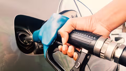 Foto: Eine Hand hält die hellblaue Zapfpistole einer Zapfsäule in den Tankstutzen eines Verbrenners.