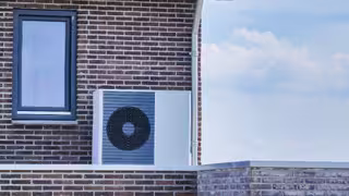 Foto: Luftwärmepumpeneinheit, die im Freien an einem modernen verklinkerten Haus installiert ist