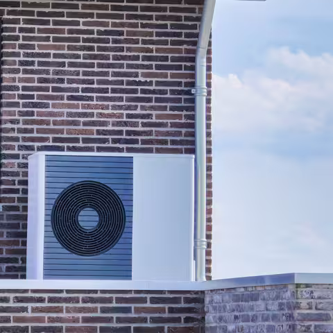 Foto: Luftwärmepumpeneinheit, die im Freien an einem modernen verklinkerten Haus installiert ist
