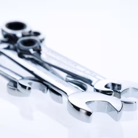 Foto: Mehrere glänzende Schraubenschlüssel unterschiedlicher Größe liegen auf weißem Untergrund übereinander.