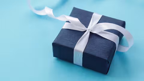 Foto: ein in dunkelblaues Papier verpacktes Geschenk mit weißer Schleife auf türkisfarbenem Grund