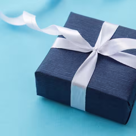 Foto: ein in dunkelblaues Papier verpacktes Geschenk mit weißer Schleife auf türkisfarbenem Grund