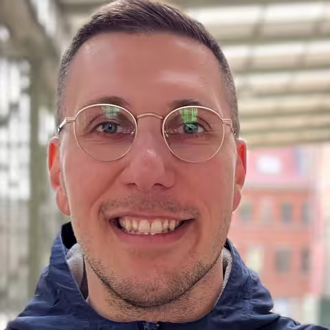 Foto: Das Bild das Portrait eines freundlichen jungen Mannes mit Brille und kurzen Haaren, der in die Kamera lächelt.