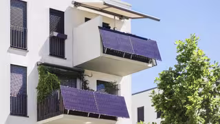 Foto: ein weißes moderndes Mehrfamilienhaus mit zwei Balkonkraftwerken vor blauem Himmel.