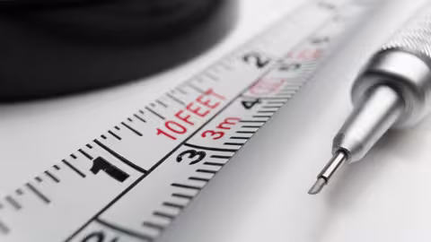 Nahaufnahme von einem Teil eines metallenen Maßbandes, neben dem ein feiner Grafitstift aus Edelstahl liegt