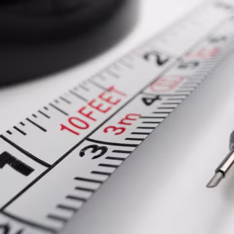 Nahaufnahme von einem Teil eines metallenen Maßbandes, neben dem ein feiner Grafitstift aus Edelstahl liegt