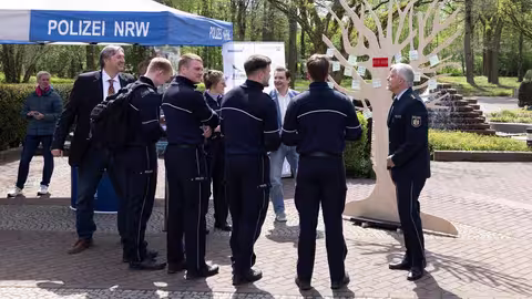 Foto: Mehrere uniformierte Polizisten und Personen in Zivil stehen an einem sonnigen Tag am Infostand der mission E im Freien.