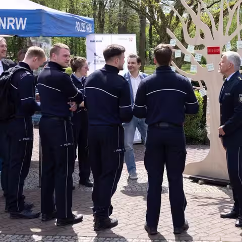 Foto: Mehrere uniformierte Polizisten und Personen in Zivil stehen an einem sonnigen Tag am Infostand der mission E im Freien.