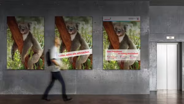 Ein verschwommen abgebildeter Mann geht an einer Wand eines Bürogebäudes vorbei, an der drei Aushänge mit einem Koala hängen.