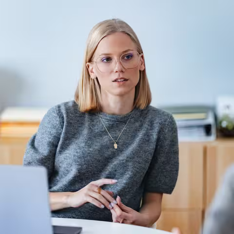 Foto aus der Perspektive der geöffneten Bürotür: Zwei Frauen unterhalten sich - die eine sitzt an ihrem Schreibtisch, die andere steht davor.