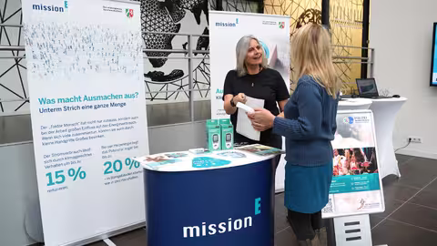 Foto: der Infostand des Landeskriminalamtes NRW mit einer Theke, zwei Roll-ups der mission E und einem Aufsteller