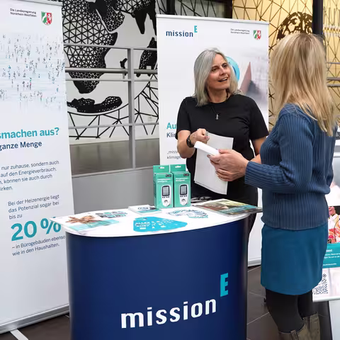 Foto: der Infostand des Landeskriminalamtes NRW mit einer Theke, zwei Roll-ups der mission E und einem Aufsteller
