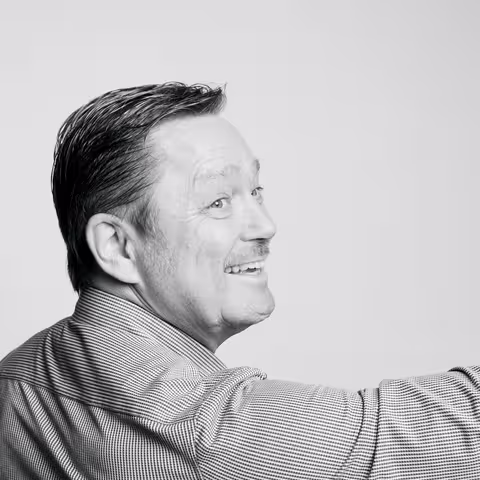 Marcel Grümmer dreht sich um, schaut über die Schulter in Richtung der Kamera und winkt lächelnd.