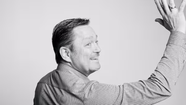 Marcel Grümmer dreht sich um, schaut über die Schulter in Richtung der Kamera und winkt lächelnd.