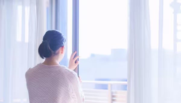 Foto: Eine junge Frau, seitlich von hinten fotografiert, öffnet ein großes Fenster.