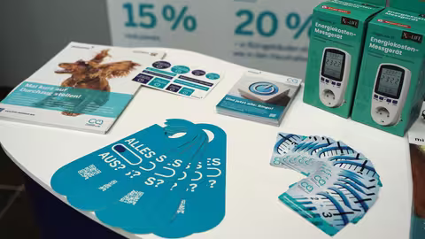 Foto: Theke eines Infostandes, auf dem mehrere Aktionsmittel liegen und auch Strommessgeräte für die Beschäftigten stehen.