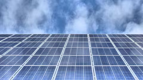 Foto: Blick von unten auf eine Solaranlage auf einem Dach, darüber der bewölkte Himmel