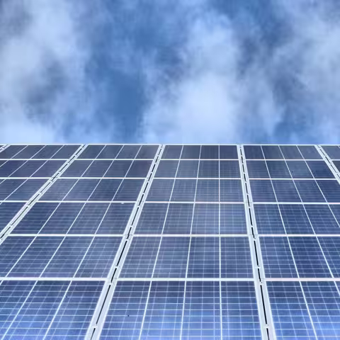 Foto: Blick von unten auf eine Solaranlage auf einem Dach, darüber der bewölkte Himmel