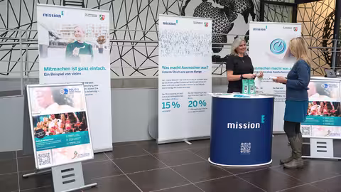 Foto: der Infostand des Landeskriminalamtes NRW mit einer Theke, mehreren Roll-ups der mission E und zwei Aufstellern zu den Energiewochen 2025