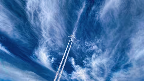Foto: ein Flugzeug mit Kondensstreifen am leicht bewölkten blauen Himmel