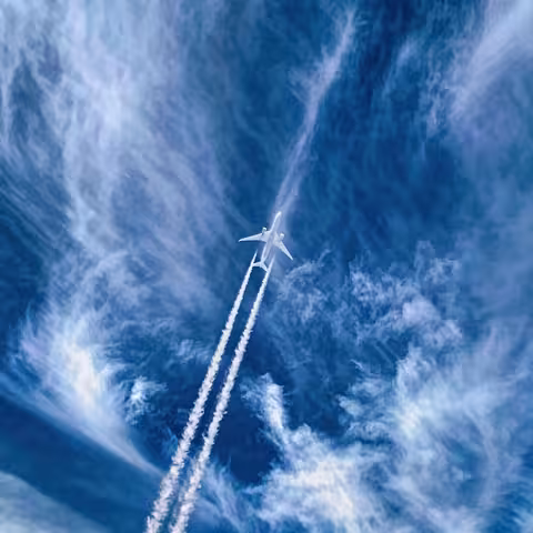 Foto: ein Flugzeug mit Kondensstreifen am leicht bewölkten blauen Himmel