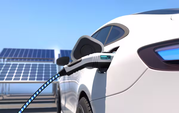Elektroauto wird über ein Ladekabel geladen; im Hintergrund stehen Solarpaneele.