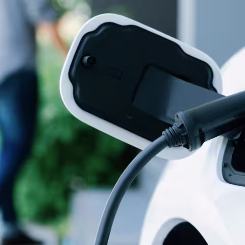 Foto: Nahaufnahme des Ladestutzens eines weißen Elektrofahrzeugs mit angeschlossenem Ladekabel