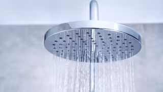 Moderne, runde Duschkopfbrause lässt Wasser in feinen Strahlen nach unten regnen.