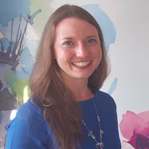 Foto: Portrait von Frau Farnung, die lange, offene braune Haare, einen blauen Pullover und eine silberne Halskette trägt.