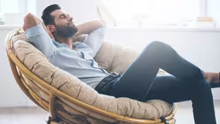 Foto: Ein junger Mann sitzt entspannt lächelnd mit geschlossenen Augen in einem Korbsessel.