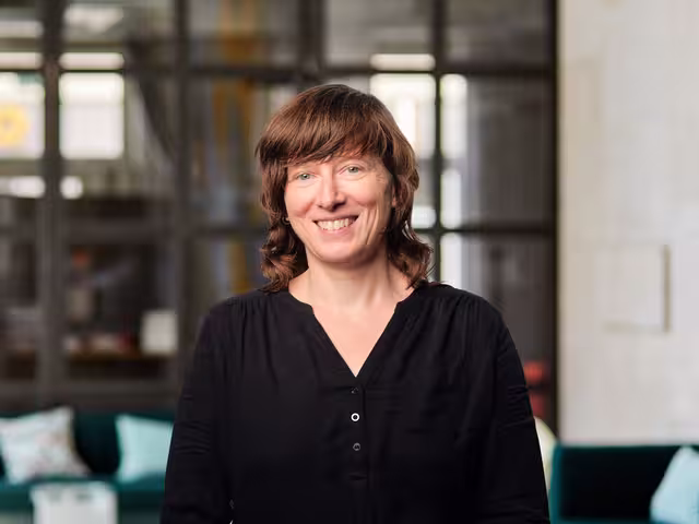 Eva Marx hat blaue Augen, trägt schulterlanges braunes Haar und eine schwarze Bluse.