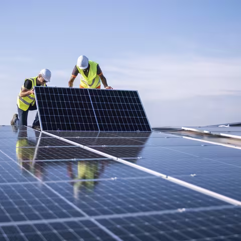 Foto: zwei Ingenieure, die Sonnenkollektoren auf einem Dach installieren