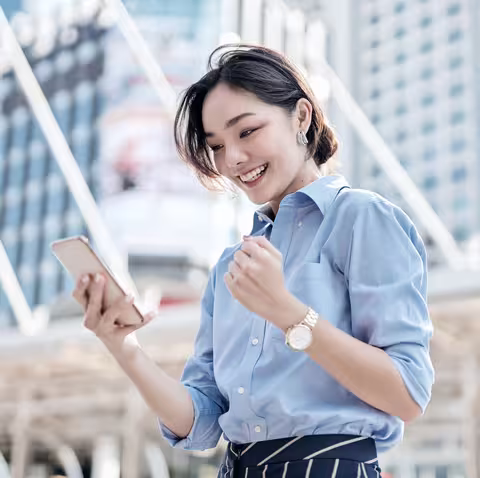 Foto: Eine junge asiatische Geschäftsfrau schaut auf ihr Smartphone und ist sehr glücklich.