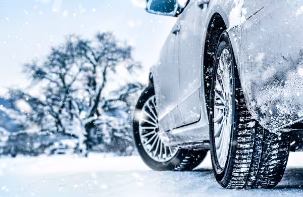 Auto fährt im Schneefall über eine verschneite Straße, Fokus auf die Reifen.