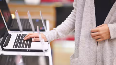 Foto: Eine junge Frau steht vor einem Notebook und legt die Finger einer Hand auf die Tastatur.