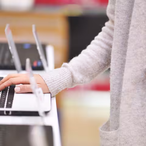 Foto: Eine junge Frau steht vor einem Notebook und legt die Finger einer Hand auf die Tastatur.