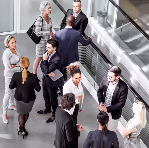 Foto: Blick von oben auf eine diverse Gruppe von Beschäftigten, die sich angeregt in mehreren kleineren Gruppen unterhalten.