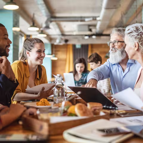 Foto: Eine Gruppe von Menschen unterschiedlichen Alters sitzen gemeinsam am Frühstückstisch und plaudern miteinander.
