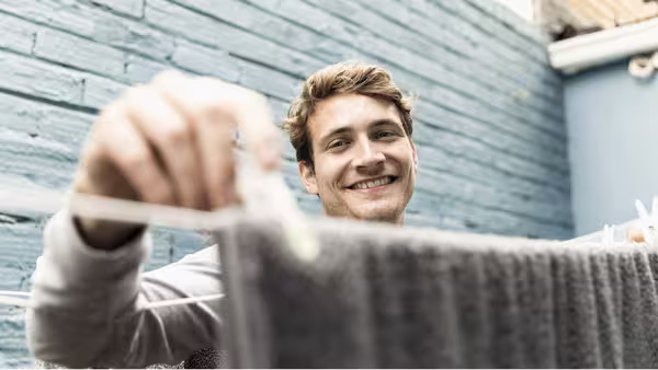 Foto: Ein junger, blonder lächelnder Mann trocknet Wäsche im Hinterhof.