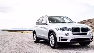 Silberner SUV steht auf einer staubigen Landstraße in einer offenen, bergigen Landschaft.