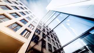 Foto: die Glasfassade eines modernen Bürogebäudes mit Blickrichtung gen Himmel.