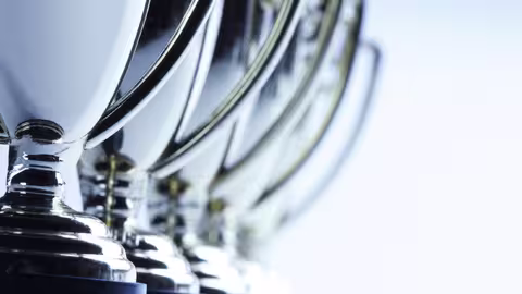 Foto: Nahaufnahme von einer Reihe hintereinander stehenden, chromblitzenden Pokalen mit seitlichem Henkel