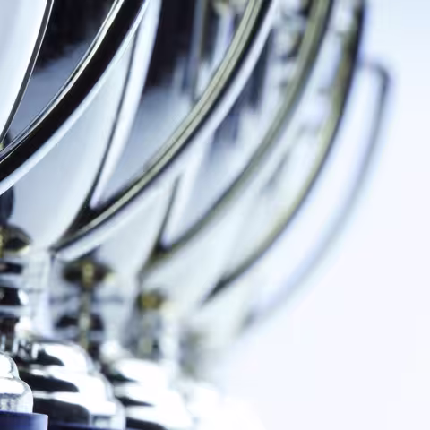 Foto: Nahaufnahme von einer Reihe hintereinander stehenden, chromblitzenden Pokalen mit seitlichem Henkel