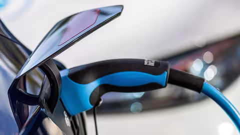 Foto: Nahaufnahme eines hellbau-schwarzen Ladessteckers im Ladestutzen eines Elektrofahrzeugs