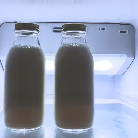 Foto: zwei volle Milchflaschen, die im oberen Regal eines beleuchteten Kühlschranks stehen